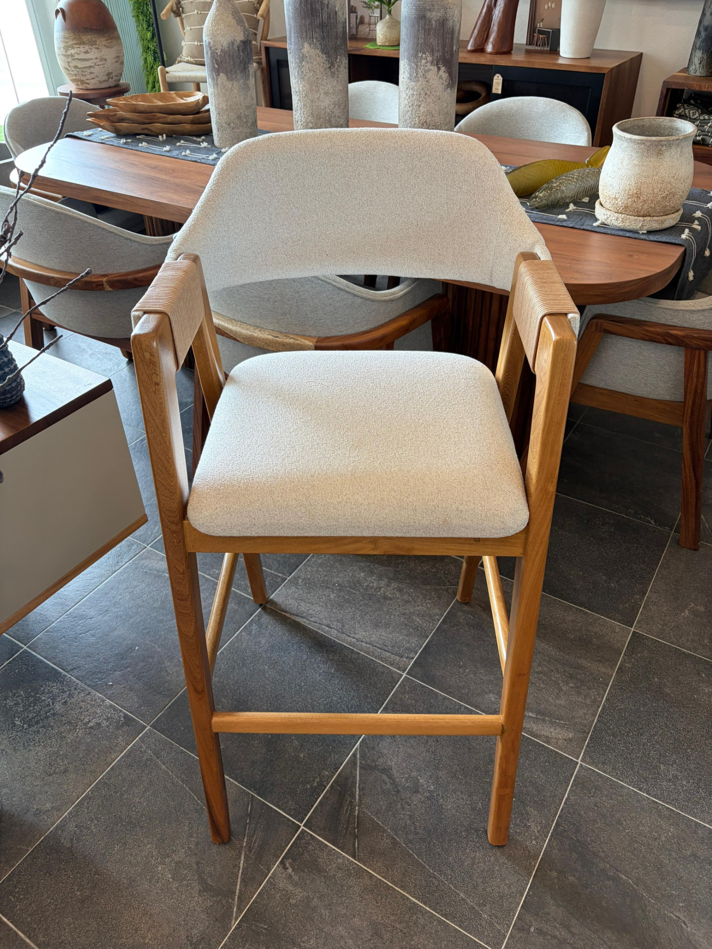 Banco alto de madera con tapicería en bouclé frente al comedor del showroom Mezquite